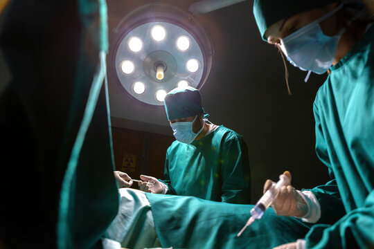 Surgeon Team Hand Scissors Injecting Medicine Working Together In Surgery Room. Group Doctor Performing Operation Giving Tools And Drug Injecting. Medical Staff Working Using Equipment Save Patient