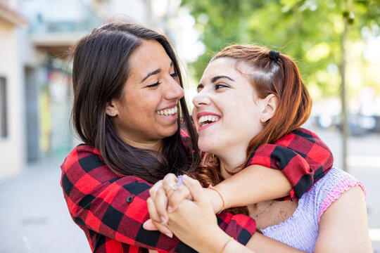 Happy woman hugging girlfriend from behind on footpath