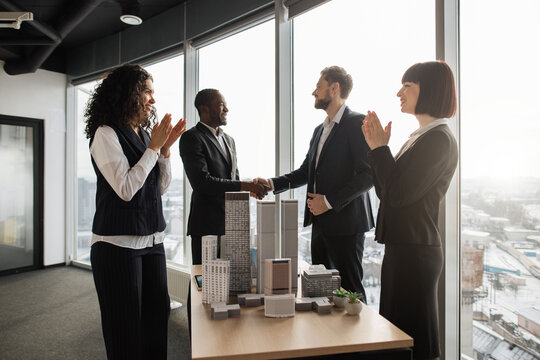 Multiethnic businesspeople real estate, agents developers handshake and applauding after successful deal of city district urban planning project good team work. Business partnership meeting concept