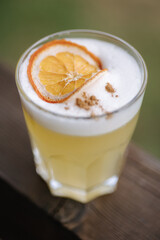 Fresh yeallow gin coctail with tonic and juice. Decorated by a slice of dried orande and cinnamon powder. Wooden table