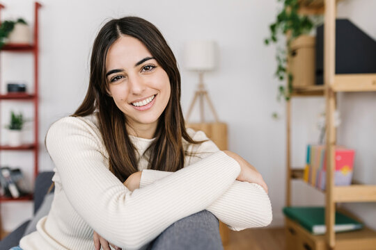 Happy young woman sitting on sofa at home