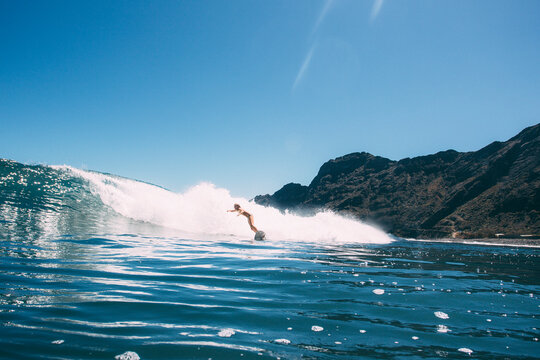 A girl surfs a wave in a bikini on a blue sky day