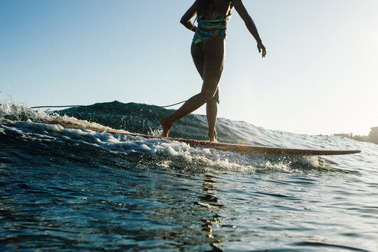 A surfer girl in a bikini surfs a little wave on her longboard during a before sunset session