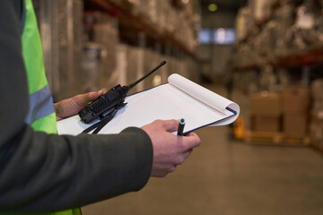 Close up of unrecognizable worker holding clipboard in warehouse with blank white mock up, copy...