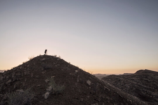 A photographer with a tripod stands on the top of a hill at sunrise in Big Bend National Park, Texas.