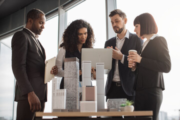 Beautiful confident curly business lady showing her financial and sales report on laptop pc for her focused high-skilled multiracial business colleagues working on city district urban planning project
