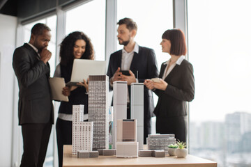 Close up of residential project maquette. Beautiful confident curly business lady showing her financial and sales report on laptop pc for her focused high-skilled multiracial business colleagues.
