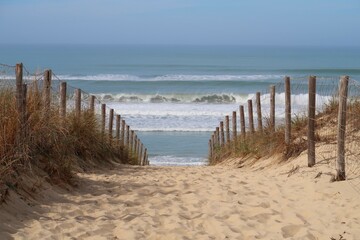 Chemin de sable cloturé par une ganivelle et descendant vers la mer et la plage des Dunes à Lège...