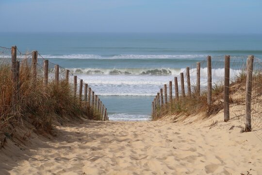 Chemin de sable cloturé par une ganivelle et descendant vers la mer et la plage des Dunes à Lège Cap Ferret, en Gironde, avec vue sur les vagues déferlantes de l'océan Atlantique (France)
