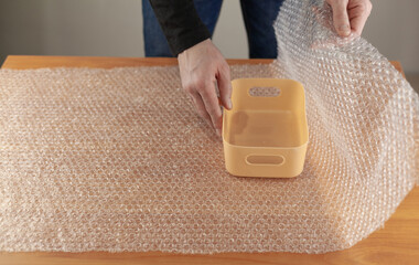 Close-up of a man's hands covering a plastic box with an air bubble wrap at a table in a warehouse