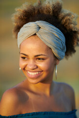 Stylish woman with brackets in band. Headshot of beautiful smiling woman with dyed hair in band and big hoops with bare shoulders smiling warmly away in sunlight.