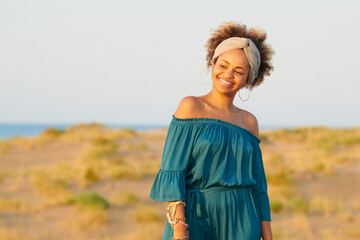 Beautiful ethnic woman on shorelines. Content modern African American women in blue dress and accessories standing on shore looking away