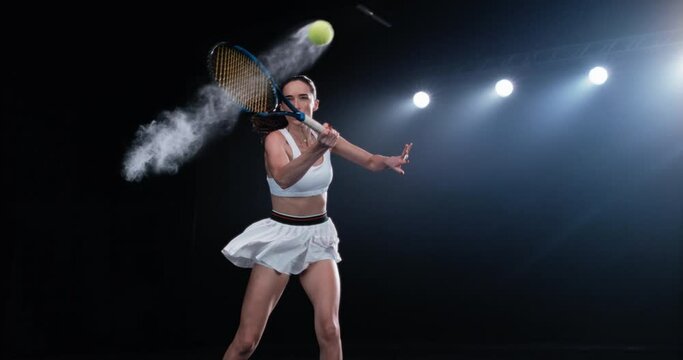Aesthetic Shot of an Athletic Female Tennis Player with a Black Background Hitting the Ball Under Spotlights. Cinematic Super Slow Motion Captures a Winning Strong Forehand Shot with Smokey Effect 