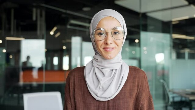 Close up portrait of smiling young muslim businesswoman employee in hijab looking at the camera in glass modern workplace Happy entrepreneur with glasses enjoying great workday in the office indoors