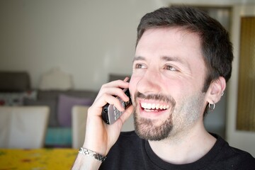 Happy man using a cordless phone to communicate with someone. The man's relaxed and cheerful expression conveys a positive message, during a social or business conversation.