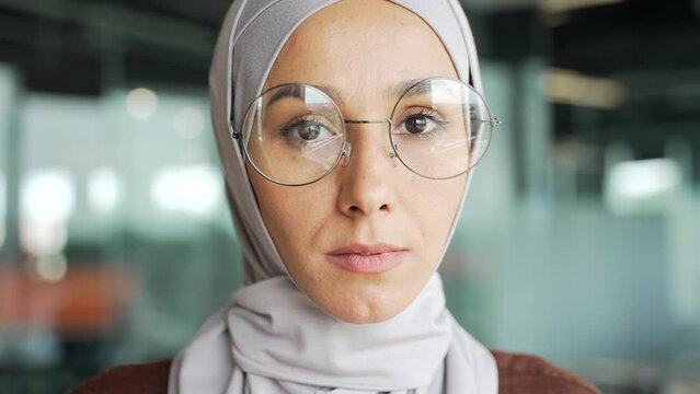 Close up portrait of serious young muslim businesswoman employee in hijab looking at the camera in glass modern workplace Head shot of calm charming entrepreneur with glasses in the office indoors