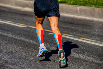 kinesio tapipng on calf muscle of athlete runner running on dark asphalt