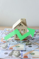 Dollar bills, a green up arrow and house on the table. The concept of the rising price of real estate.