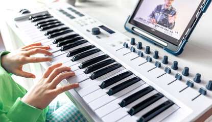 Fototapeta na wymiar Little girl learns to play the piano with online, distance learning music.