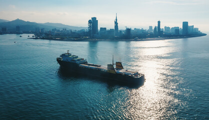 Cargo freight ship with containers and trucks sailing to industrial logistic port, aerial view from drone.