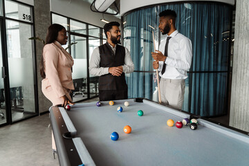 Young multiracial people in suits playing pool at office lobby