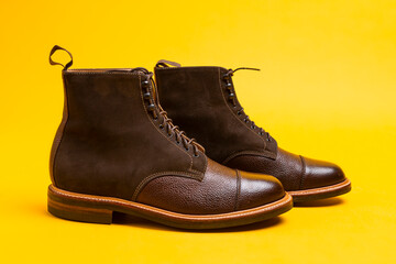 Premium Dark Brown Grain Brogue Derby Boots Made of Calf Leather with Rubber Sole Placed Over One Another On Yellow Background.