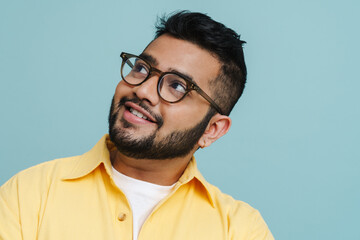 Obraz premium Smiling indian guy looking away while posing isolated over blue wall