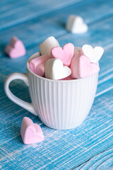 A cup with heart-shaped marshmallows, close-up on a blue wooden background.