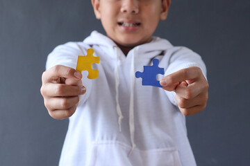 Colorful puzzle pieces holded by hands of young boy isolated on gray background. Autism awareness,...