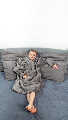 Fototapeta premium A six-year-old boy of European appearance is dressed in gray pajamas, lying and having fun on a gray bed.