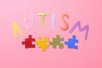 Colorful autism lettering with colorful puzzle isolated on pink background. World Autism Awareness Day.