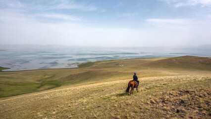 shepherd riding his horse on the meadow near a lake in Kyrgyztan
