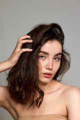 Fototapeta premium Curly heatlhy hair. Portrait of young beautiful brunette girl with well-kept skin over grey studio background. Concept of natural beauty, skincare, cosmetology, plastic surgery, health