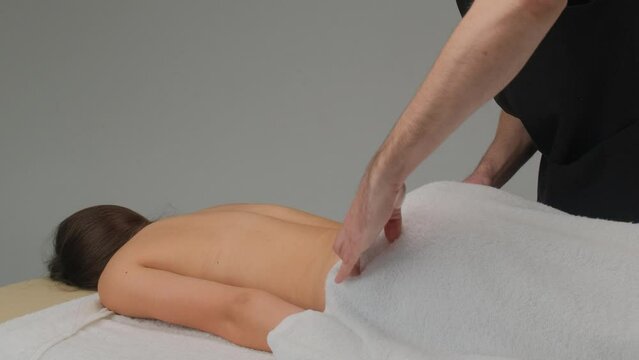 The masseur covers the lower part of the body of a young girl with a white towel before the massage. Slow-motion footage.