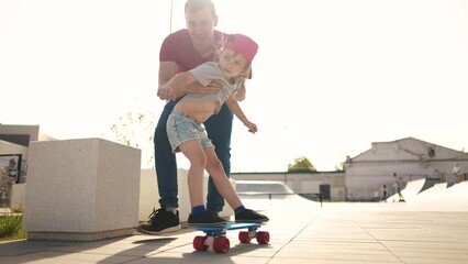 learn to skateboard. dad teaches daughter to ride a skateboard outdoors at the playground. father and daughter play training concept. lifestyle parent teaching child daughter to skateboard - Powered by Adobe