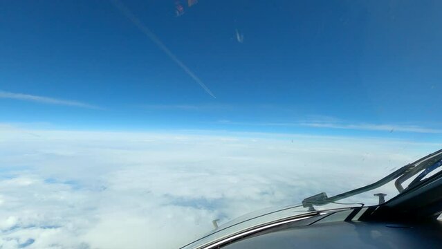 Contrail in blue sky as airplane flies at elevation above clouds; aircraft POV