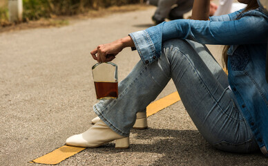 Drunk driver woman holding alcohol bottle sitting on road after car accident 