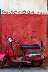 Fototapeta premium Cute red motor scooter parked against a red painted wall in the Islamic quarter of Cairo near the Khan el Khalili Bazaar, Egypt.