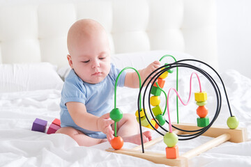 funny baby boy in blue bodysuit playing with wooden toy on bed