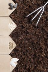 Brown paper bags with seeds on a soil. Sunflower, cucumber, tomato and pumpkin seeds. Rake for...