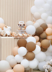 Creative gender neutral baby shower or birthday decoration in the garden. Bohemian style outdoor event set up with balloons. White cream peach caramel balloon arch kit. Sweet table for a party
