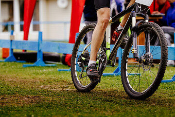 legs young cyclist riding mountain bike on field of green grass