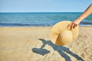 Fototapeta na wymiar Woman hold in hand straw hat on yhe beach near sea