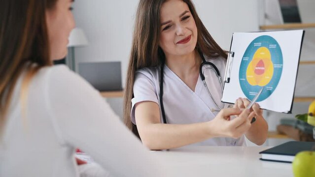 Holding illustration with nutrition data. Young woman have a consultation by female nutricionist in the clinic.
