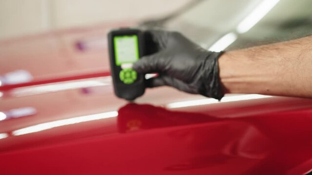 Closeup view of male hand, using film coating thickness gauge device to check car paint. Auto coating quality control. Inspector measuring paint cover thickness at the vehicle detailing service.