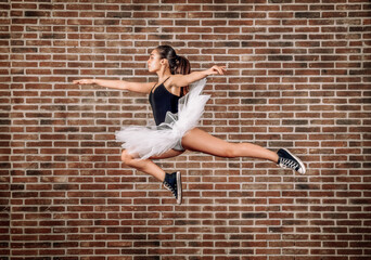 Young ballerina leaping against brick wall