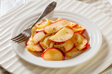 fried onion and red apple slices on white plate with fork on white wood table, horizontal view from above