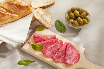 salami fine slices with bread and olives. sausage and herbs on a wooden board. snack on a light...