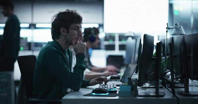 Handsome Software Developer Working on Computer in a Technological Laboratory Environment. Young Man is Thoughtful at His Workplace, Drafting Research Ideas for an AI Development Blockchain