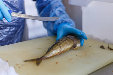 A fish factory worker cuts smoked mackerel into pieces with a knife.